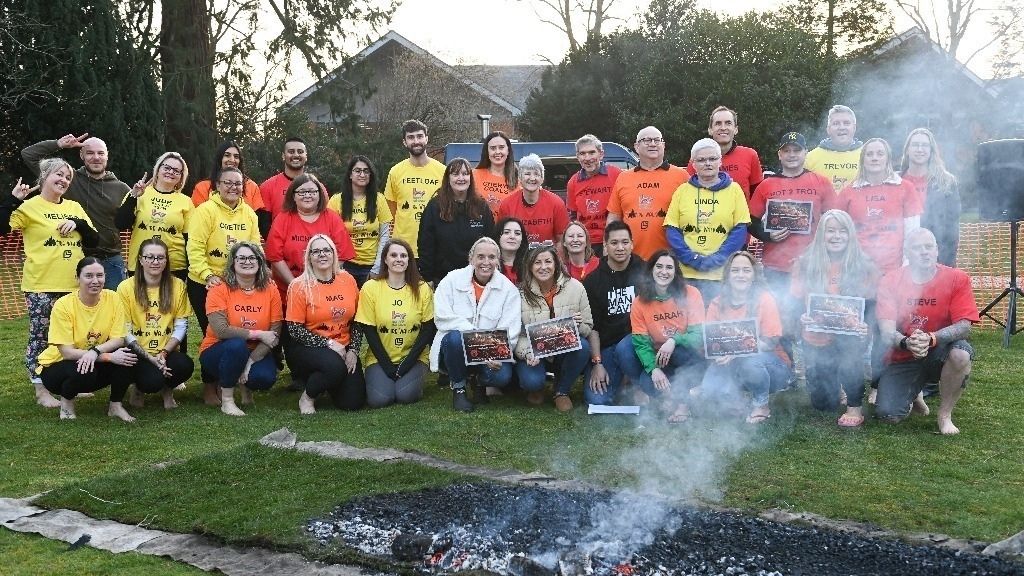 Stepping Up for Bereaved Children: Peach Care Services Proudly Partners with Harry’s Rainbow 2 A large group of fundraisers wearing colourful t-shirts gathering behind a bed of smoking coals at the Harry's Rainbow charity firewalk event.